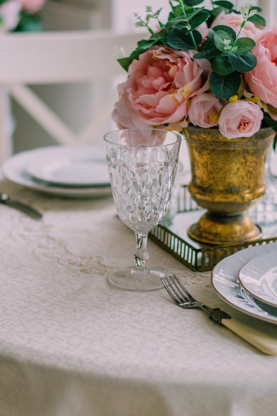 Λευκό τραπεζομάντηλο στρωμένο σε στρόγγυλο τραπέζι με σκεύη και βάζο με τριαντάφυλλα στην μέση