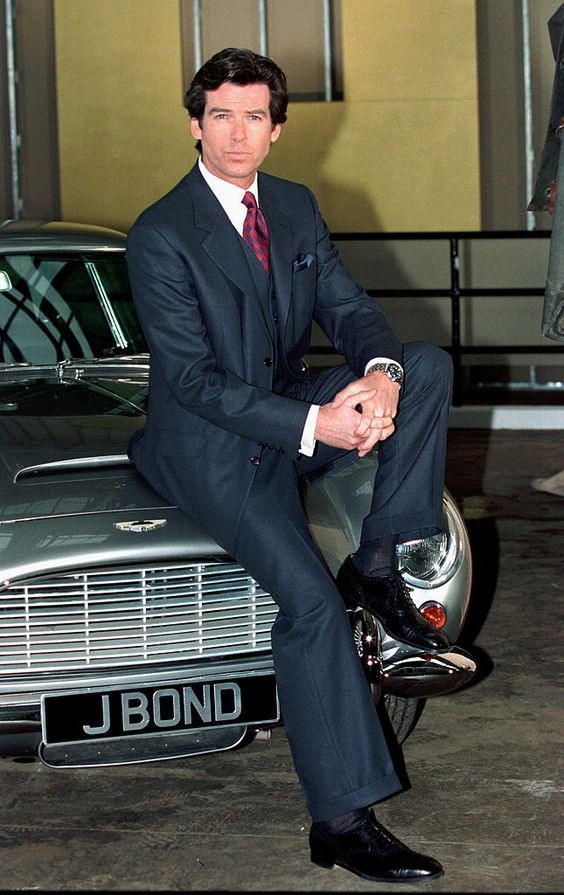 Ο Pierce Brosnan ως James Bond ποζάρει φορώντας κουστούμι Brioni καθισμένος στο μπροστινό μέρος μιας Aston Martin